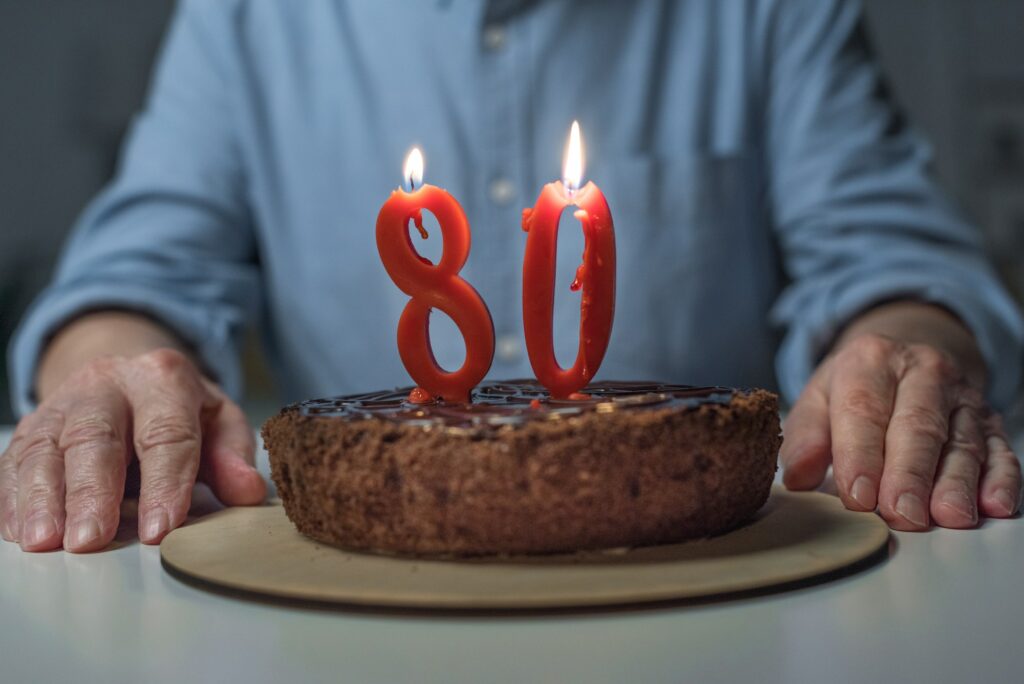 Close-up view of senior man celebrating 80 anniversary with cake and burning number candles